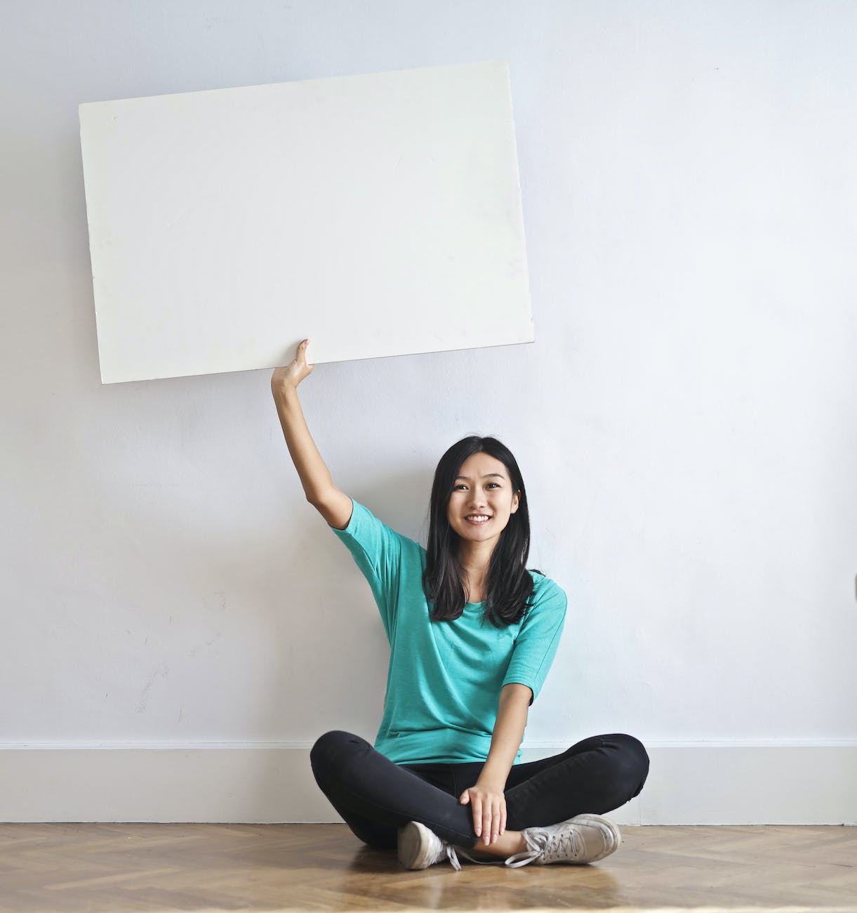 smiling ethnic woman with blank poster in empty flat