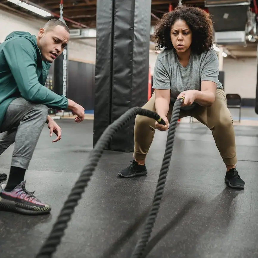 concentrated black woman exercising with battle ropes in contemporary gym