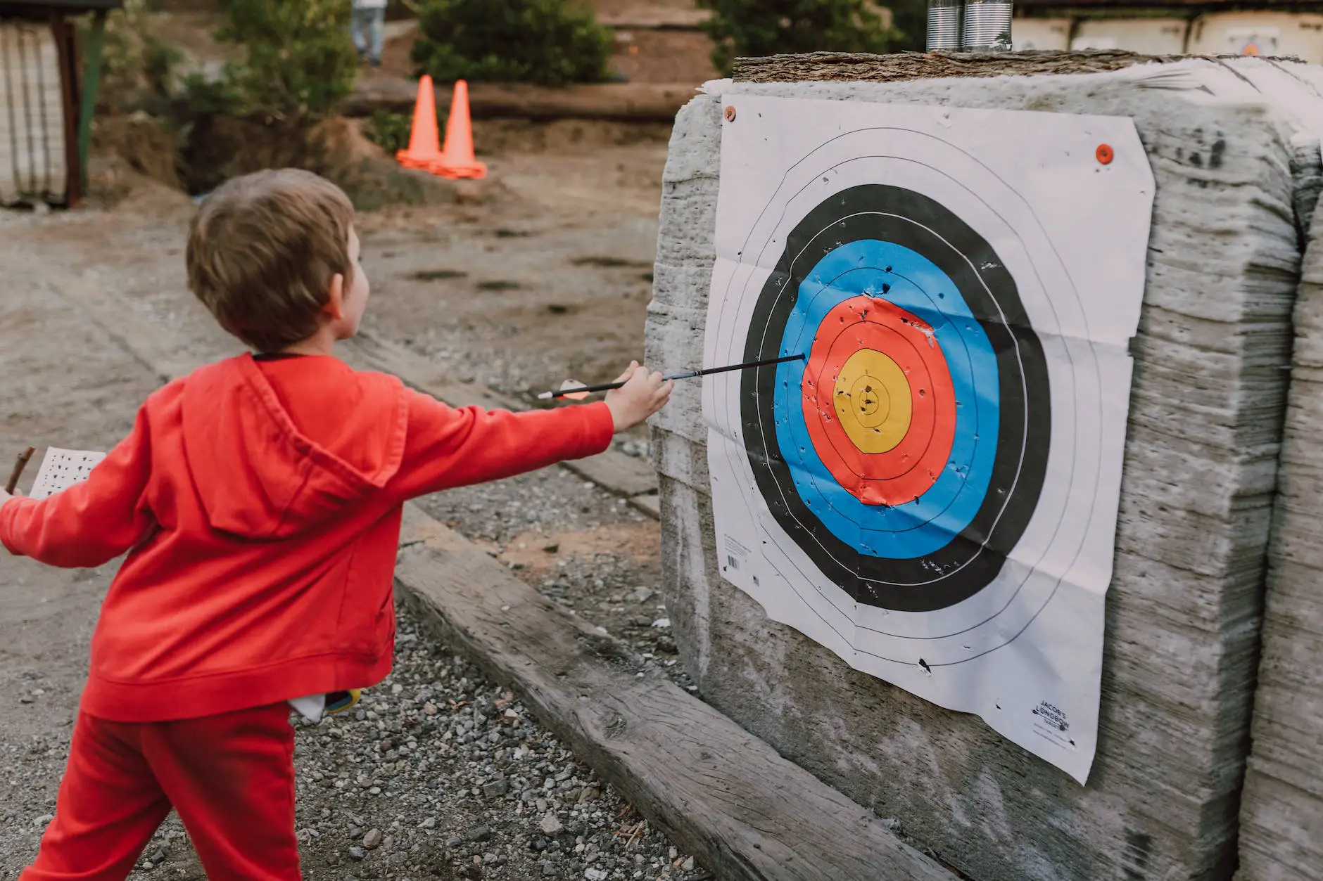 a kid in red hoodie jacket pulling out an arrow from the target